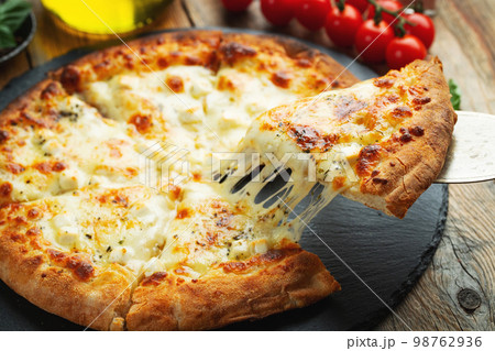 A slice of hot Italian pizza with stretching cheese. Pizza four cheeses with basil. 98762936