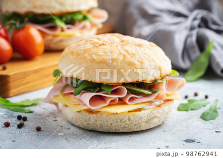 Two homemade sandwiches with ham, cheese and arugula on a concrete table. Two homemade sandwiches with ham, cheese and arugula on a concrete table. 98762941