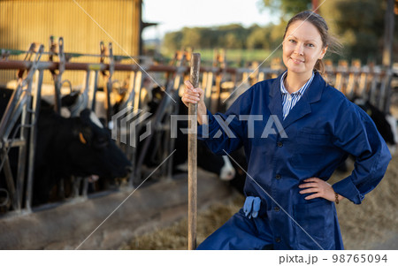 Successful woman farmer standing in cowshed at dairy cow farm 98765094