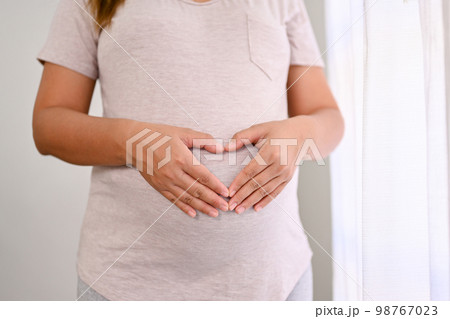 Cropped shot of a pregnant woman making heart hands sign on her big belly. love, expectation Cropped shot of a pregnant woman making heart hands sign on her big belly. love, expectation 98767023