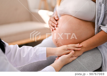 A female doctor reassuring and comforting a pregnant woman by holding her hand A female doctor reassuring and comforting a pregnant woman by holding her hand 98767069
