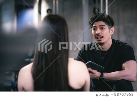 ジムでカウセリングをしているパーソナルトレーナーと女性 98767958