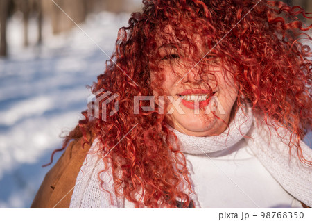 Portrait of a smiling chubby red-haired woman on a walk in winter. 98768350