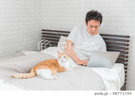 家の寝室・ベッドルームで猫・ペットと一緒にテレワーク・リモートワークする男性 家の寝室・ベッドルームで猫・ペットと一緒にテレワーク・リモートワークする男性 98771744