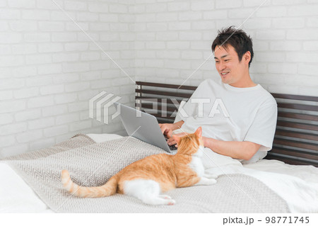 家の寝室・ベッドルームで猫・ペットと一緒にテレワーク・リモートワークする男性 家の寝室・ベッドルームで猫・ペットと一緒にテレワーク・リモートワークする男性 98771745