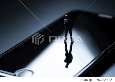 スマートフォンの上にミニチュアのビジネスパーソン スマートフォンの上にミニチュアのビジネスパーソン 98772712