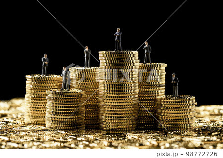 高く積み重ねたコインの上にミニチュアのビジネスパーソン 98772726