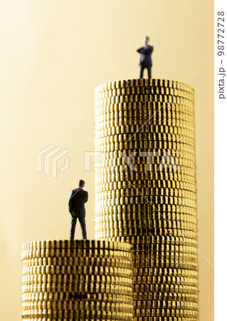 高く積み重ねたコインの上にミニチュアのビジネスパーソン 98772728