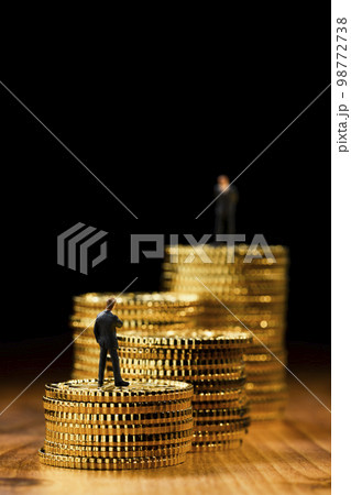 階段状に積み重ねたコインの上にミニチュアのビジネスパーソン 98772738
