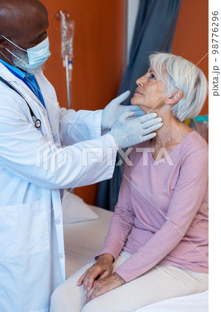 Vertical of diverse senior male doctor examining the throat of senior female patient, copy space Vertical of diverse senior male doctor examining the throat of senior female patient, copy space 98776296