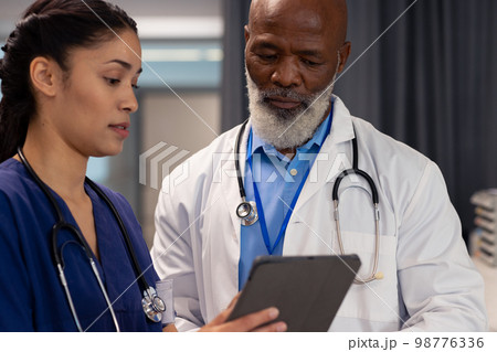 Diverse female and senior male doctor using tablet and talking in hospital, copy space 98776336
