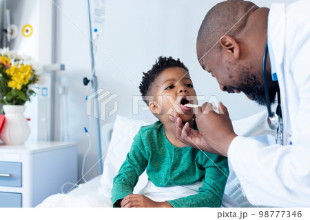 African american male doctor examining mouth of boy patient in hospital 98777346