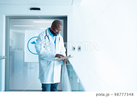 Serious african american male doctor reading notes in hospital corridor with copy space 98777348