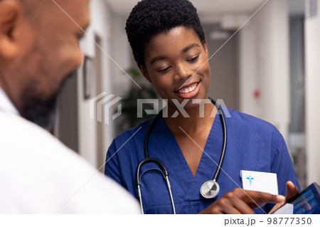 Smiling african american male and female doctor using tablet in hospital corridor 98777350
