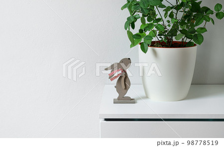 Easter bunny statuette near a plant ina white flower pot on a shelf, easter minimal concept, copy space Easter bunny statuette near a plant ina white flower pot on a shelf, easter minimal concept, copy space 98778519
