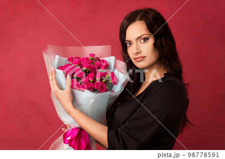 A beautiful young woman is holding a bouquet of pink roses on a pink background 98778591