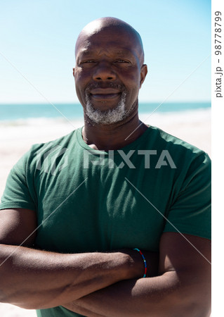 Portrait of bald confident african american senior man with arms crossed at beach under clear sky Portrait of bald confident african american senior man with arms crossed at beach under clear sky 98778799