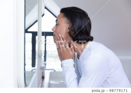 Biracial man looking in mirror in bathroom Biracial man looking in mirror in bathroom 98779171