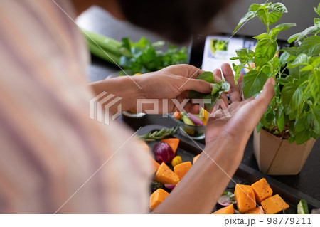 Midsection of biracial man cooking, seasoning vegetables in kitchen 98779211
