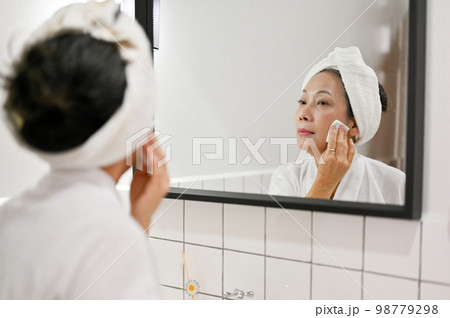 Attractive mature aged Asian woman removing makeup, looking in the mirror. beauty night routine Attractive mature aged Asian woman removing makeup, looking in the mirror. beauty night routine 98779298