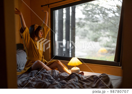 Woman wakes up in tiny bedroom of wooden cabin on nature Woman wakes up in tiny bedroom of wooden cabin on nature 98780707