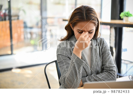 Stressed and frustrated millennial Asian businesswoman sits at her office desk 98782433