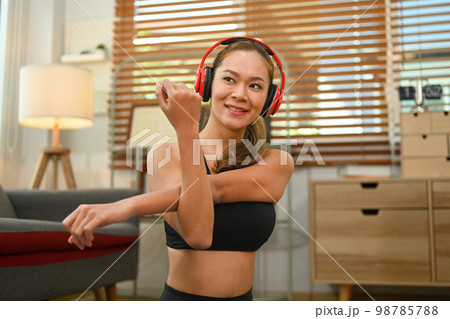 Sporty woman in headphone stretching her arms before working out at home. Fitness and healthy lifestyle concept Sporty woman in headphone stretching her arms before working out at home. Fitness and healthy lifestyle concept 98785788