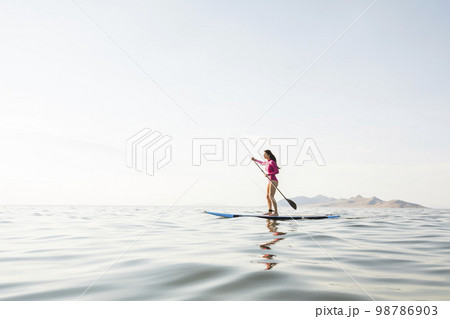 Woman in pink swimsuit paddleboarding on lake 98786903