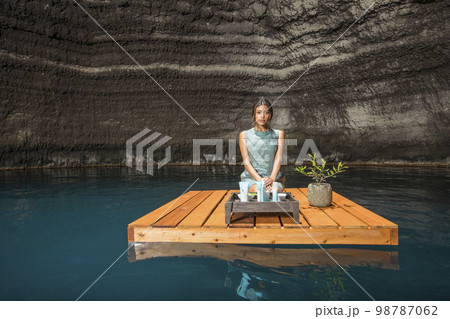 Beautiful woman kneeling on wooden raft on pond Beautiful woman kneeling on wooden raft on pond 98787062