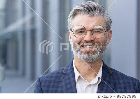 Successful gray haired man in business suit close up, portrait of mature businessman with beard and glasses, banker investor smiling and looking at camera from outside office building boss satisfied. 98787999