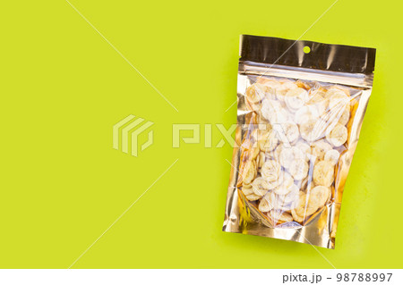 Banana slice chips in package bag on green background. 98788997