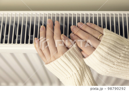 Female hands on a heating radiator, close-up. 98790292