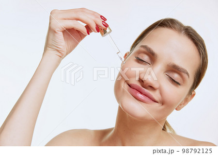 Portrait of young beautiful girl with clear face applying face serum, taking care after skin condition over grey studio background. Concept of natural beauty, cosmetology Portrait of young beautiful girl with clear face applying face serum, taking care after skin condition over grey studio background. Concept of natural beauty, cosmetology 98792125