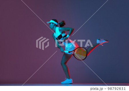Portrait of young professional female tennis player in sports uniform in motion, action over gradient pink-purple background in neon light. Sport, fashion, energy, motivation concept Portrait of young professional female tennis player in sports uniform in motion, action over gradient pink-purple background in neon light. Sport, fashion, energy, motivation concept 98792631