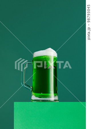 Anise taste. Mug with foamy green beer isolated over green background. Concept of st patrick's day celebration, brewery, traditions Anise taste. Mug with foamy green beer isolated over green background. Concept of st patrick's day celebration, brewery, traditions 98793045