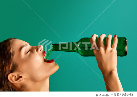 Woman pouring green beer into her mouth over green studio background. Concept of st patrick's day celebration, brewery, traditions, Woman pouring green beer into her mouth over green studio background. Concept of st patrick's day celebration, brewery, traditions, 98793048