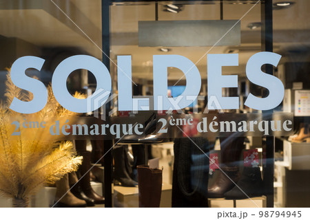 Closeup of discount sign "SOLDES deuxieme demarque, troizieme demarquej" in french,  the traduction of  (sales second set in english) on the window of fashion store 98794945