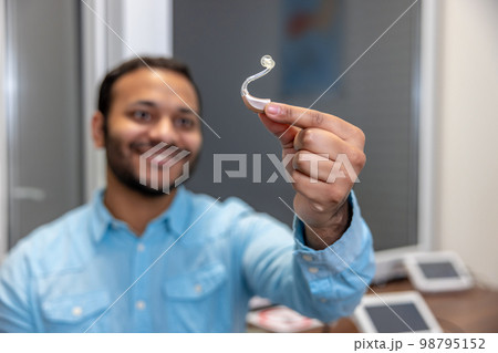 Smiling young man holding a hearing aid 98795152