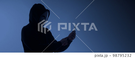 Hacker Anonymous and face mask with smartphone in hand. Man in black hood shirt holding and using mobile phone on white background. Represent cyber crime data hacking or stealing personal data concept 98795232