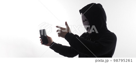 Hacker Anonymous and face mask with smartphone in hand. Man in black hood shirt holding and using mobile phone on white background. Represent cyber crime data hacking or stealing personal data concept 98795261