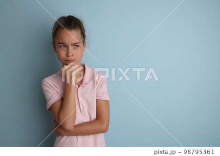 Little emotional teenage girl in pink shirt 11, 12 years old on an isolated blue background. Children's studio portrait. Place text to copy space for caption, advertising children's goods. 98795361