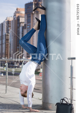 beautiful slender woman business manager or lawyer or politician or official in Friday less formal dress code practices yoga headstand pose in lunch time outside office for relaxation at summer sun 98795949