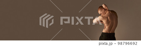 Relief, strong, muscular male back. Young man posing shirtless in pants over light brown studio background. Banner. Men's health, beauty and sportive lifestyle 98796692