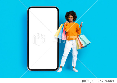 Cool black woman with shopping bags posing by big phone 98796864