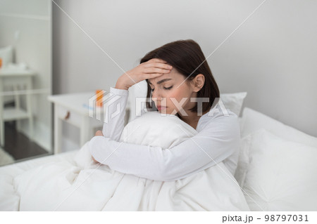 Sick woman sitting in bed, touching head, copy space 98797031