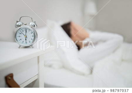 Alarm clock over stressed woman lying in bed at home Alarm clock over stressed woman lying in bed at home 98797037