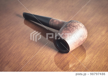 A wooden smoking pipe lies on a varnished table close up A wooden smoking pipe lies on a varnished table close up 98797486