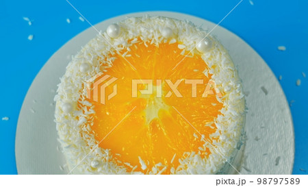 Cake with orange and coconut shavings spinning on a blue background. 98797589
