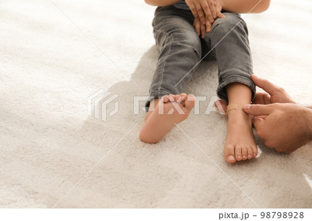 Father putting sticking plaster onto little son's leg indoors, closeup Father putting sticking plaster onto little son's leg indoors, closeup 98798928