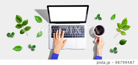 Person using a laptop computer with green leaves 98799487